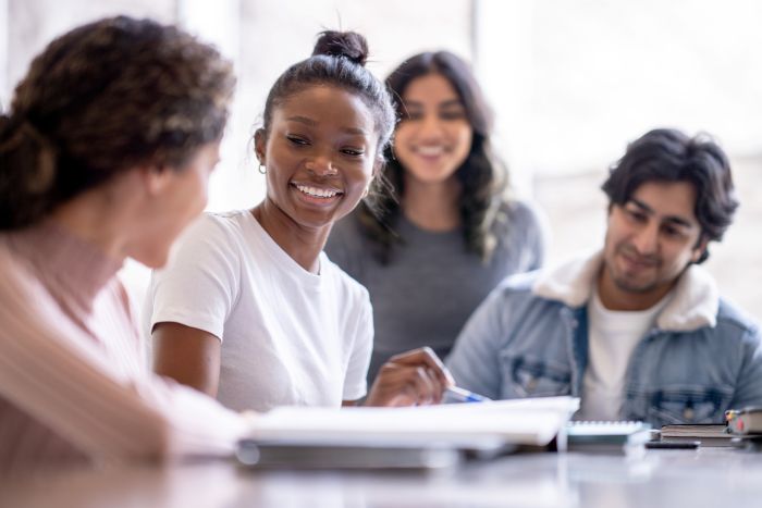 A group of young adults smiling while conversing around notebooks