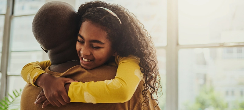 A young girl with curly hair smiles while hugging her father