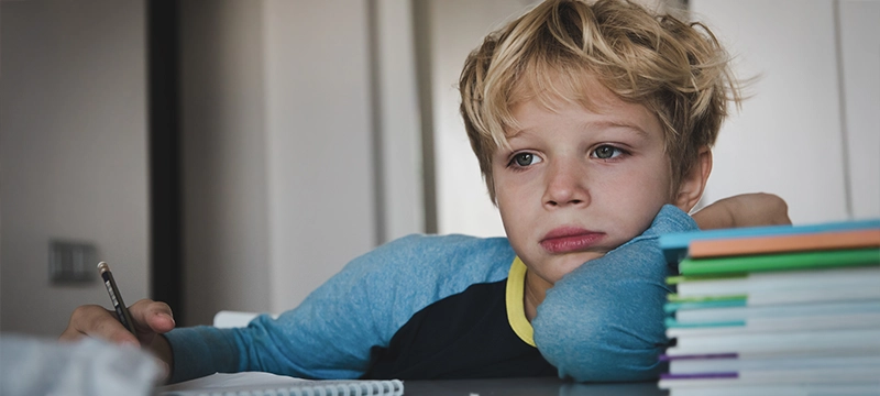 A young blonde boy looks emotionally upset while trying to do schoolwork
